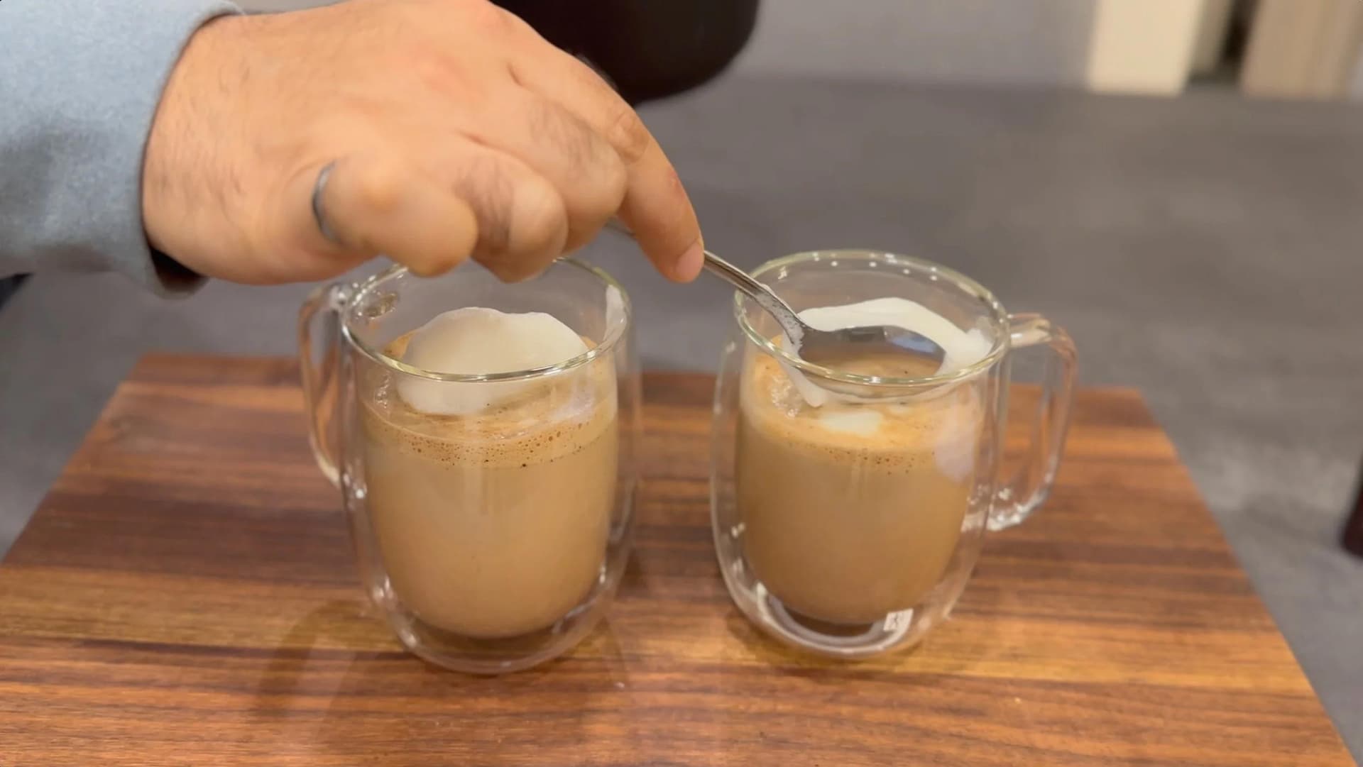 Two glass mugs of chocolate cappuccino with layered steamed milk and foam, hand pouring milk into one cup.