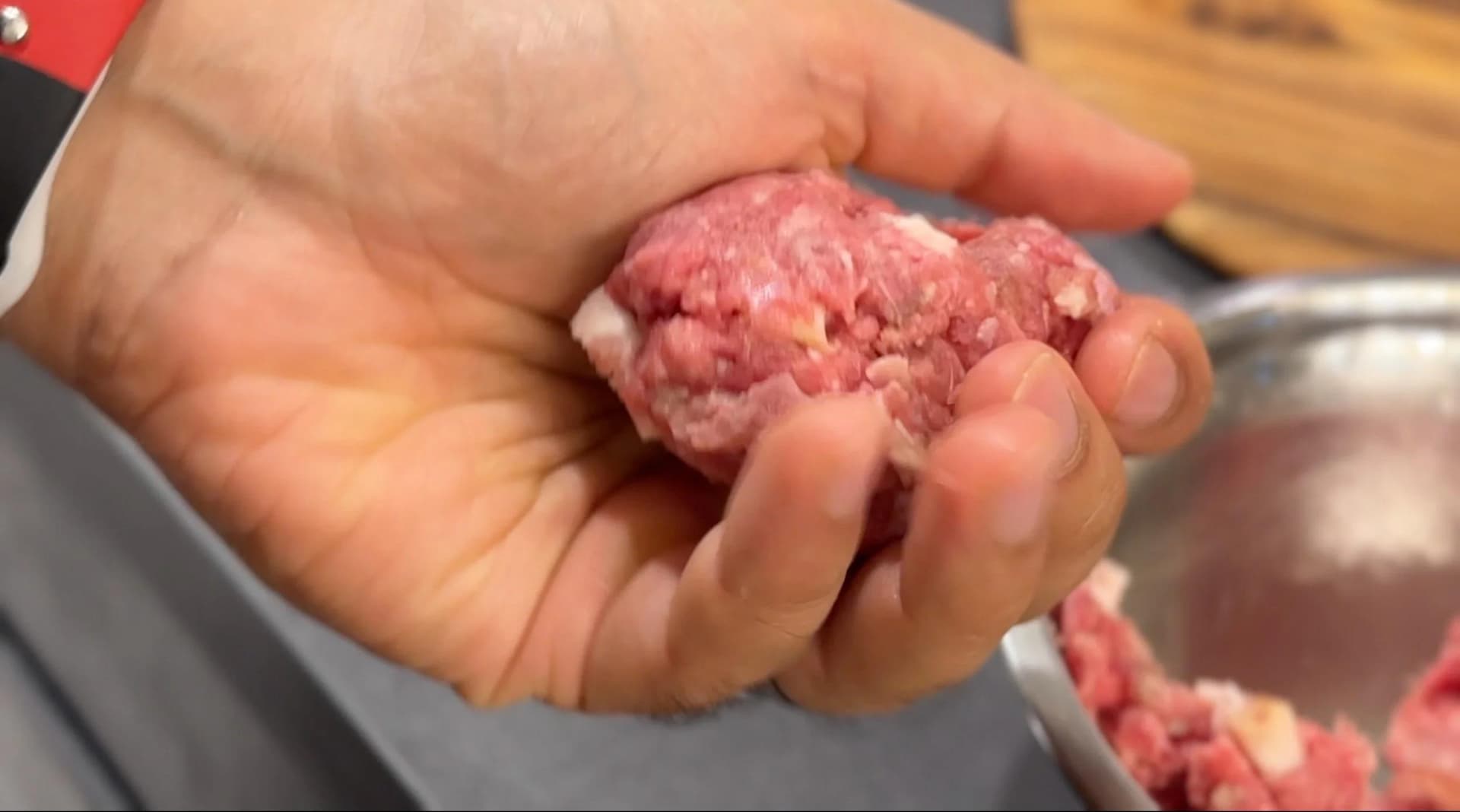 Hand holding a formed ground beef patty ball with bacon and seasonings mixed in