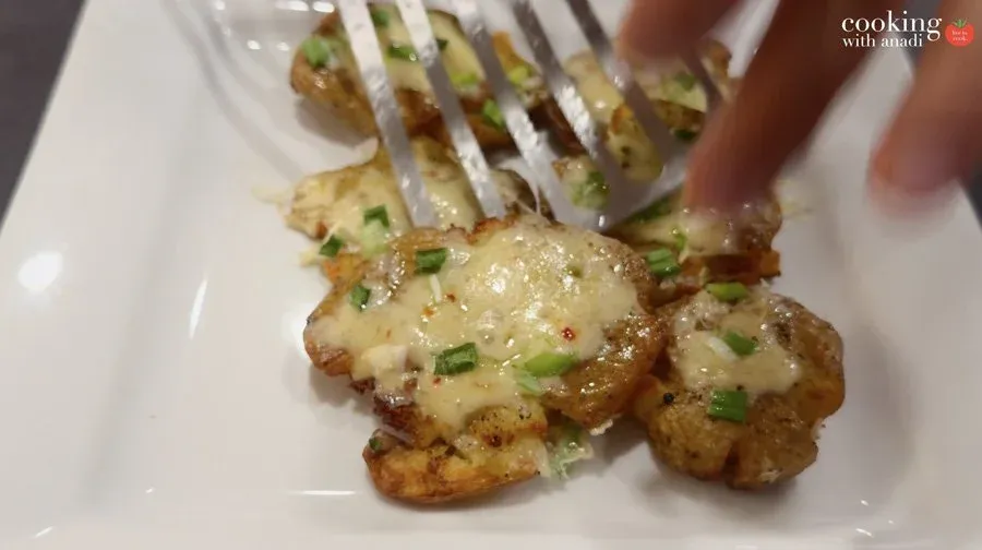 Crispy air fryer smashed potatoes topped with melted cheese and chopped green onions on a white plate with a fork.