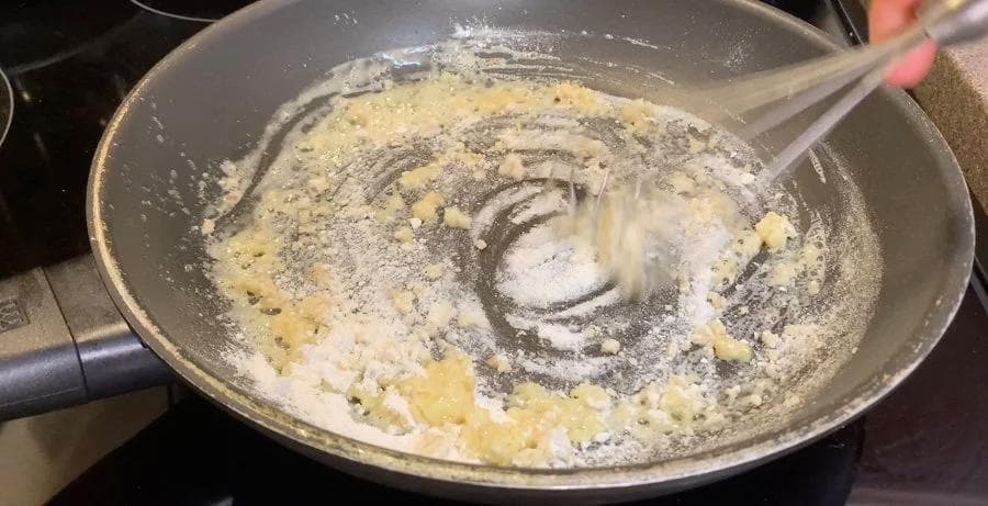Roux cooking in a skillet with butter, garlic, and flour being whisked together on the stovetop.