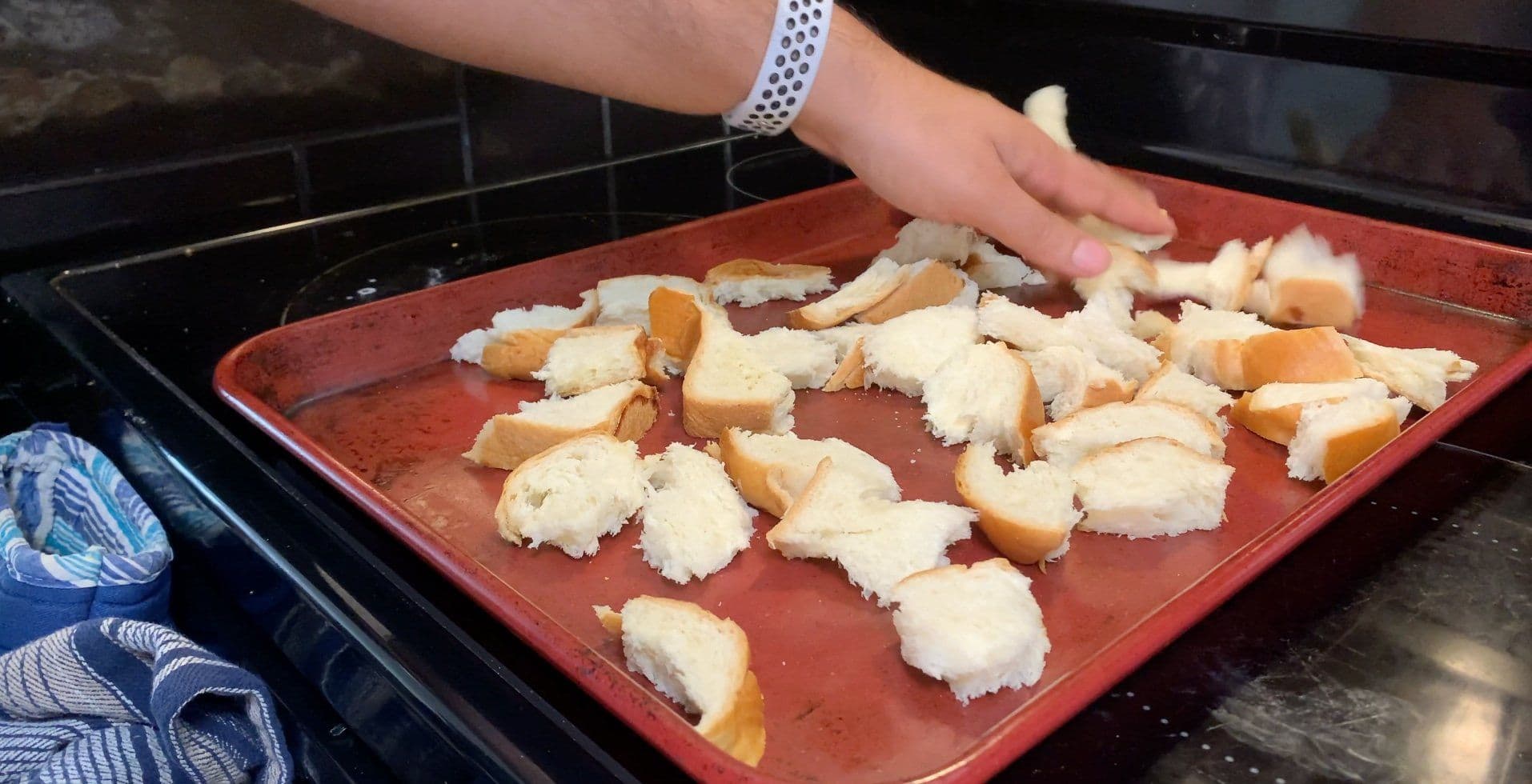 Torn brioche bread cubes spread on a red baking sheet, lightly toasted and ready for bread pudding.
