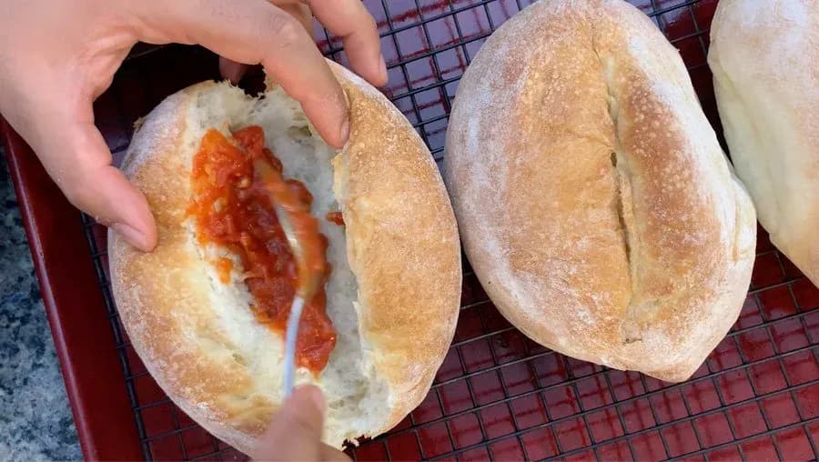 Hand holding an open Italian sub roll filled with melted cheese and red marinara sauce over a wire rack.