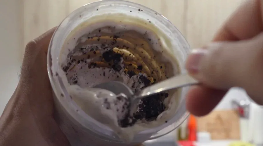 High protein Oreo ice cream mixture in a clear container with a spoon, showing creamy texture with cookie pieces.