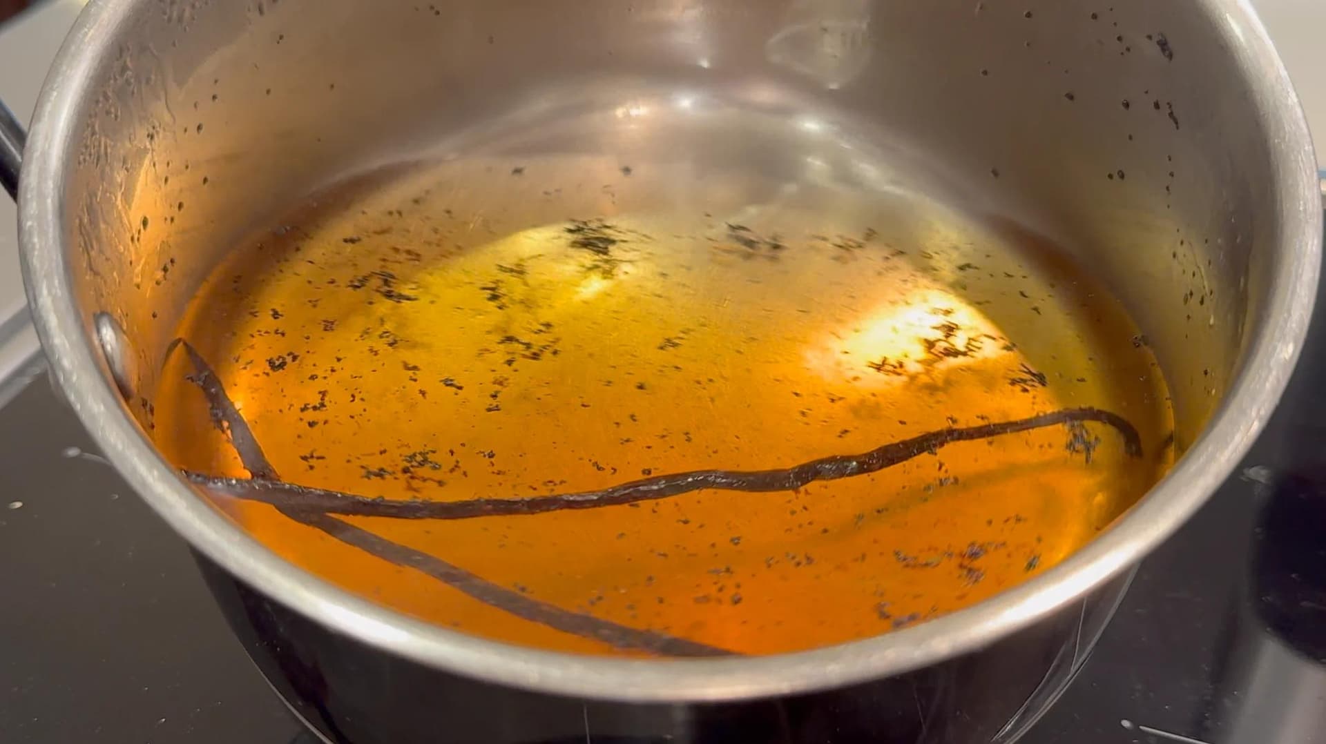 Vanilla syrup infusing in a pot with a vanilla bean pod, golden liquid with black specks.