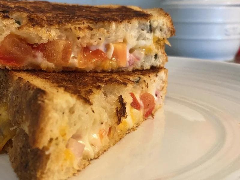 Indian grilled cheese sandwich cut diagonally, showing melted cheese, tomato, and ham between toasted bread slices on a white plate.