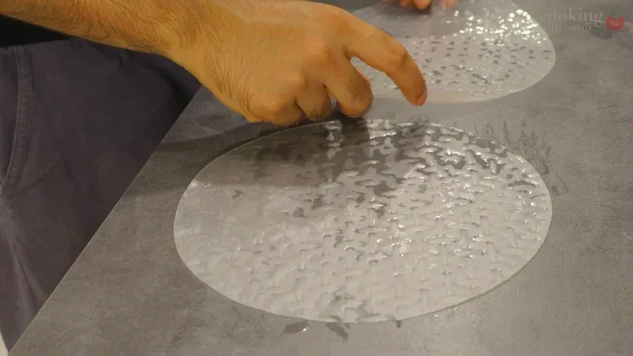 Hand dipping rice paper wrapper in water on a gray surface to soften it for filling.