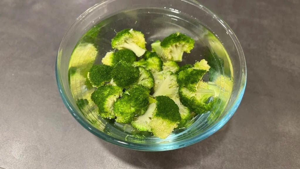 Broccoli florets cooling in an ice water bath in a glass bowl.