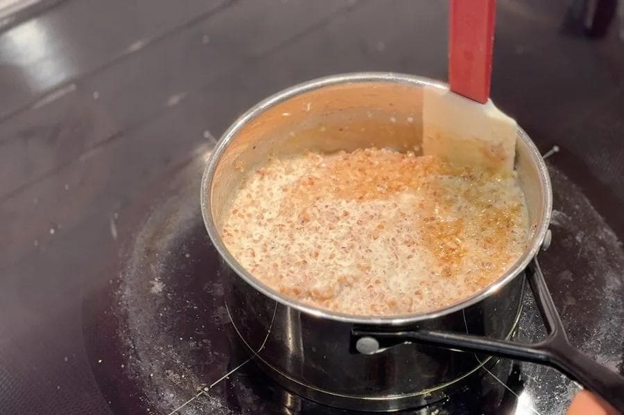 Cracked wheat porridge simmering in a silver pot on the stovetop with a red handle visible.