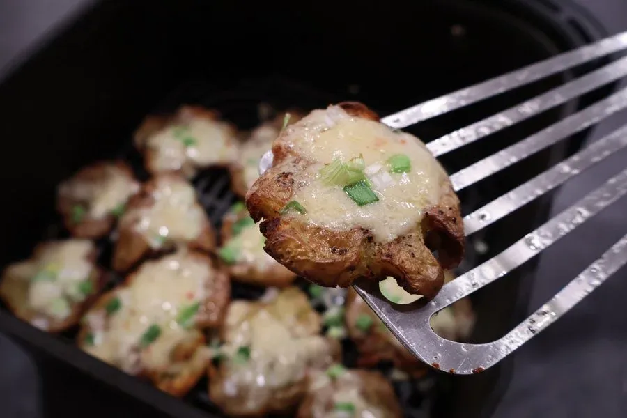 Crispy air fryer smashed potato held on fork, topped with melted cheese and green onions