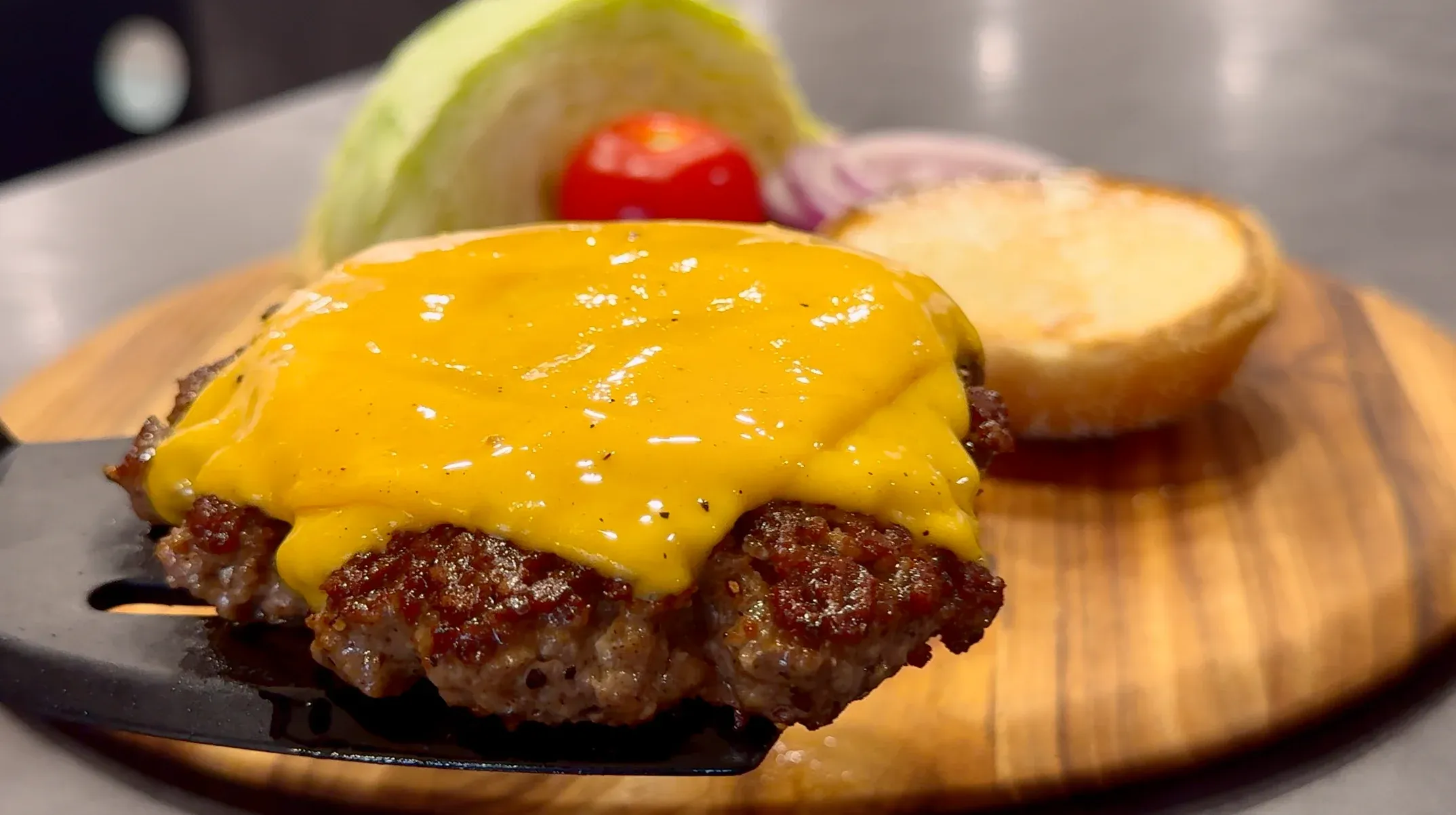 Classic cheeseburger with melted yellow cheese on toasted bun, served with lettuce, tomato, and pickles on wooden board.