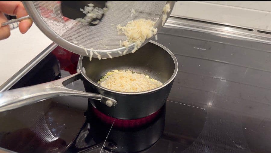Rice being poured from a colander into a black pot with sautéed garlic on a stovetop.