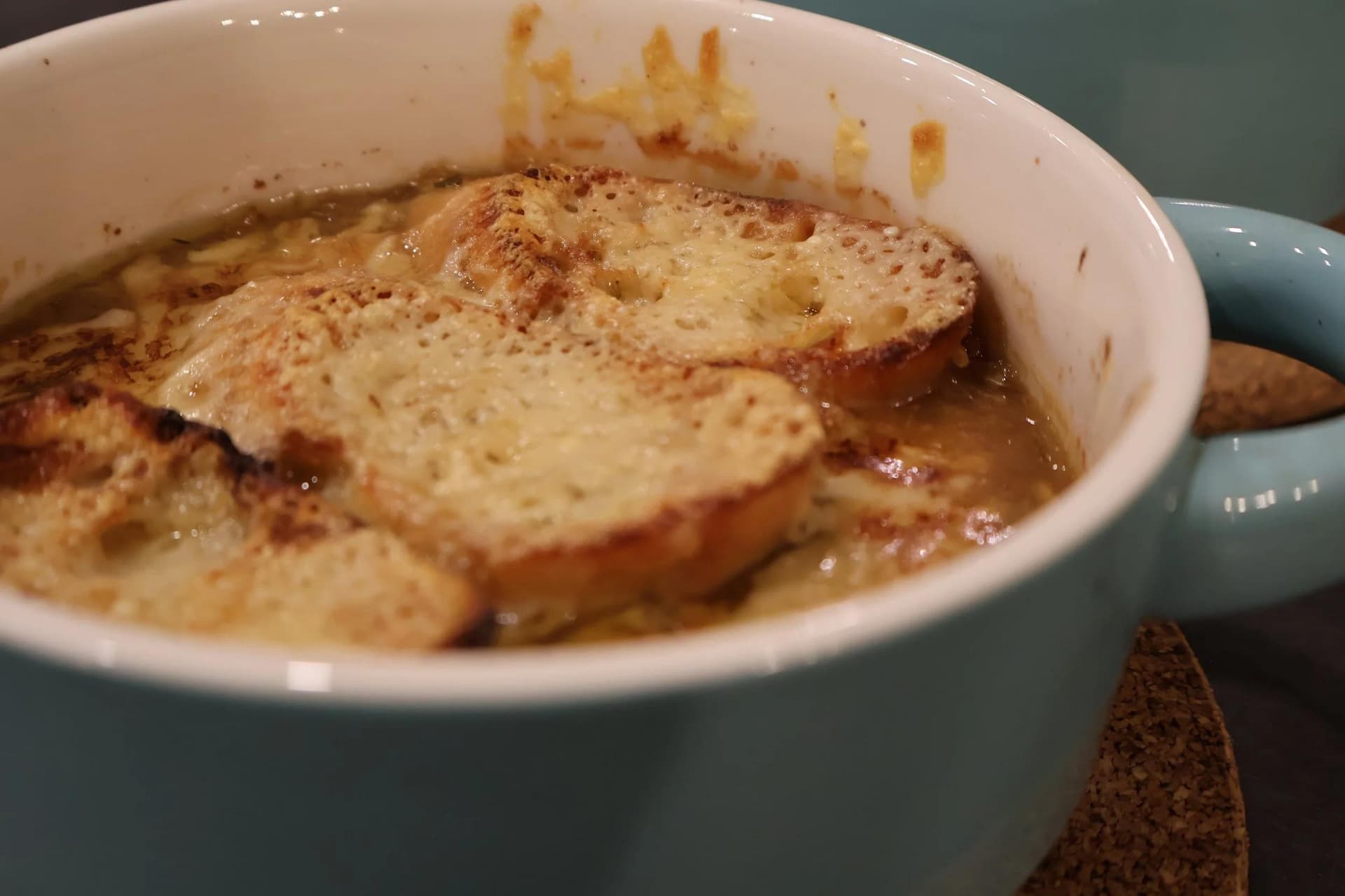 French onion soup in a teal bowl with melted cheese and toasted bread garnished with cinnamon.