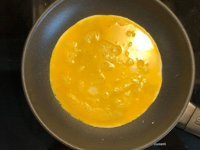 Whisked eggs cooking in a non-stick pan, partially set with a glossy golden surface.