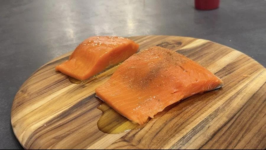 Two salmon fillets seasoned with blackening spice on a wooden cutting board, ready for air frying.
