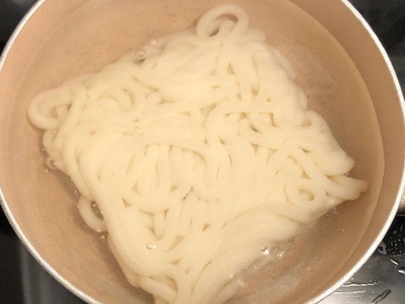 Cooked udon noodles in a pot of boiling water during preparation for teriyaki shrimp stir fry.