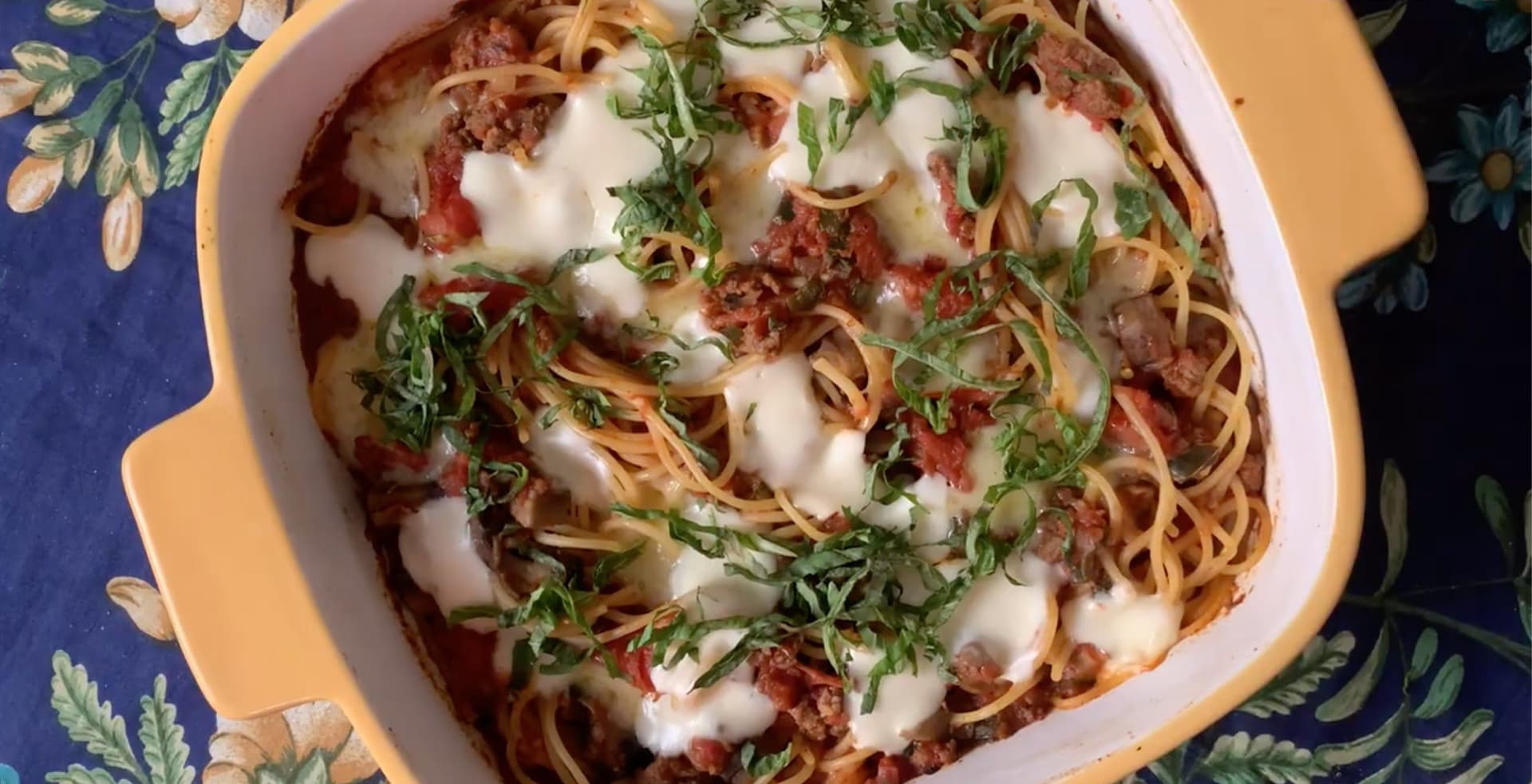Baked spaghetti casserole with melted mozzarella and cheddar cheese, topped with fresh basil and tomato sauce.