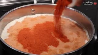 Red deggi mirch powder being sprinkled into a creamy tomato-based dal masala in a pan on the stove.