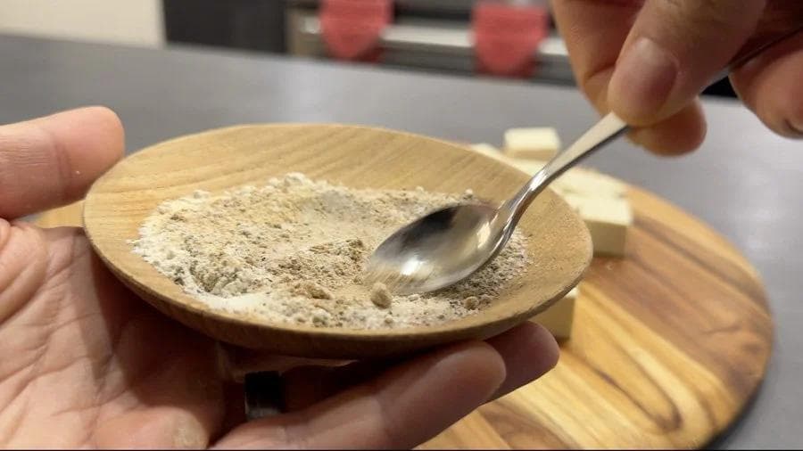 Wooden spoon mixing spice blend of ginger powder, garlic powder, onion powder, salt, pepper, and cornstarch in a small wooden bowl.