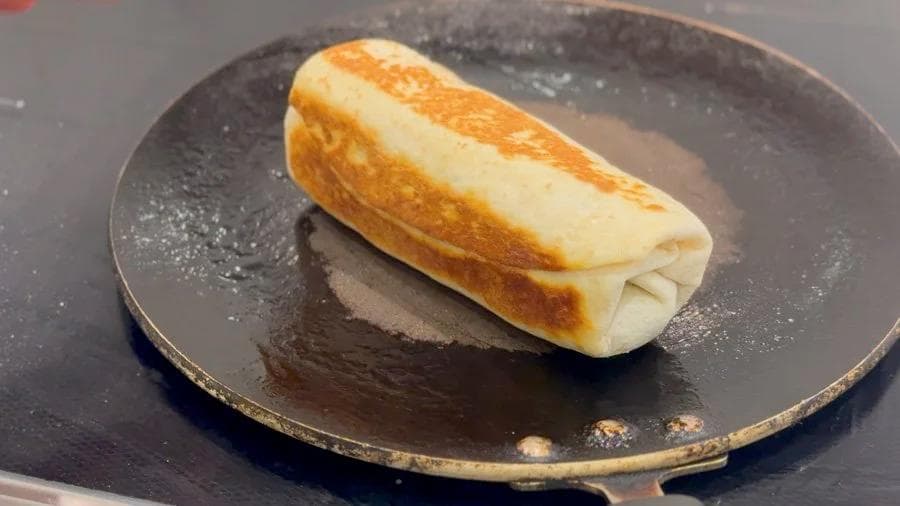 Golden-brown toasted breakfast burrito on a dark skillet, wrapped and ready to serve.