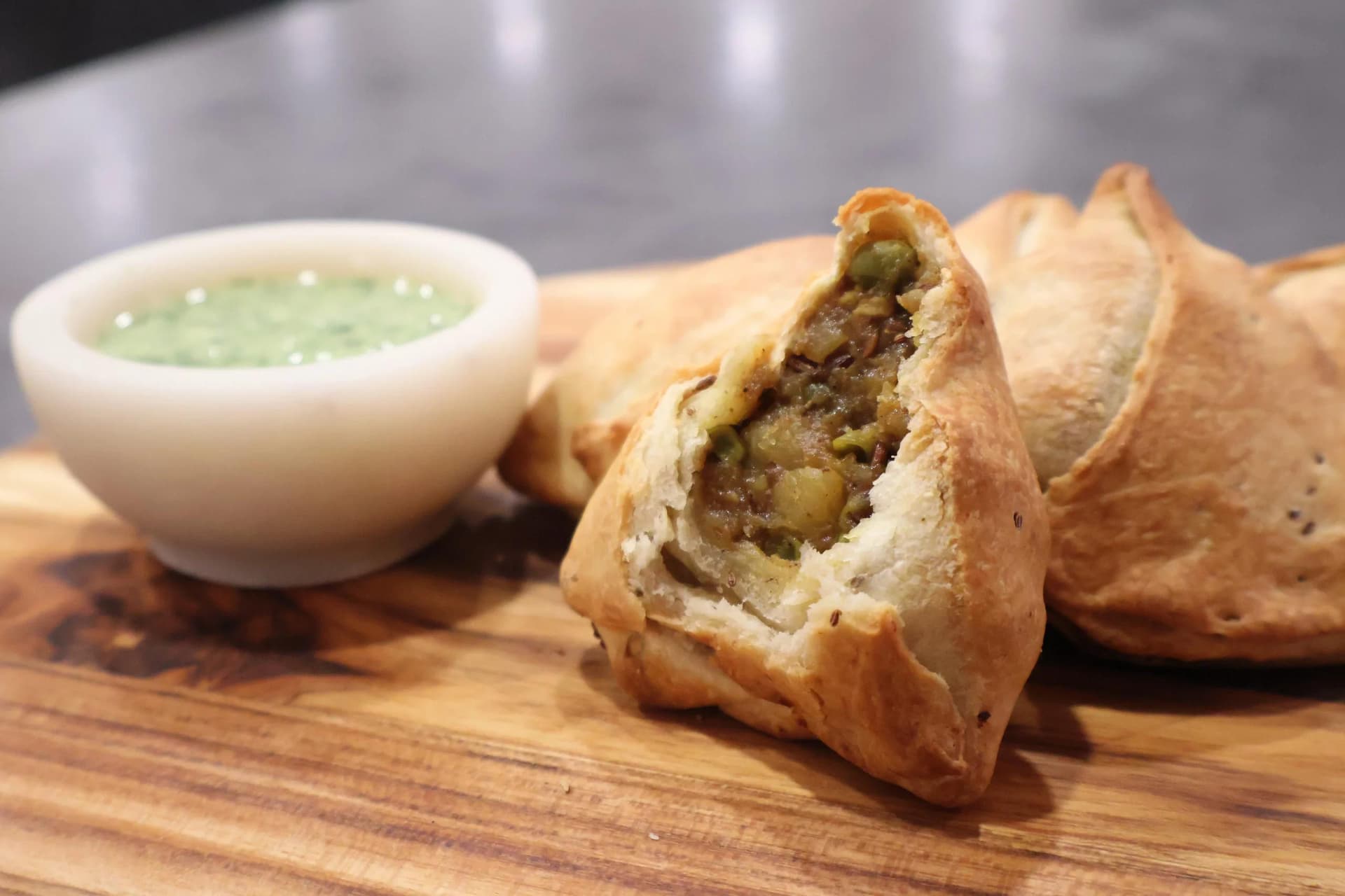 Golden air fryer samosas on wooden board with green cilantro dipping sauce in white bowl.