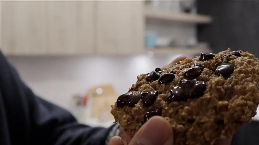 Hand holding a warm pumpkin chocolate chip cookie with melted chocolate chips visible on its surface.