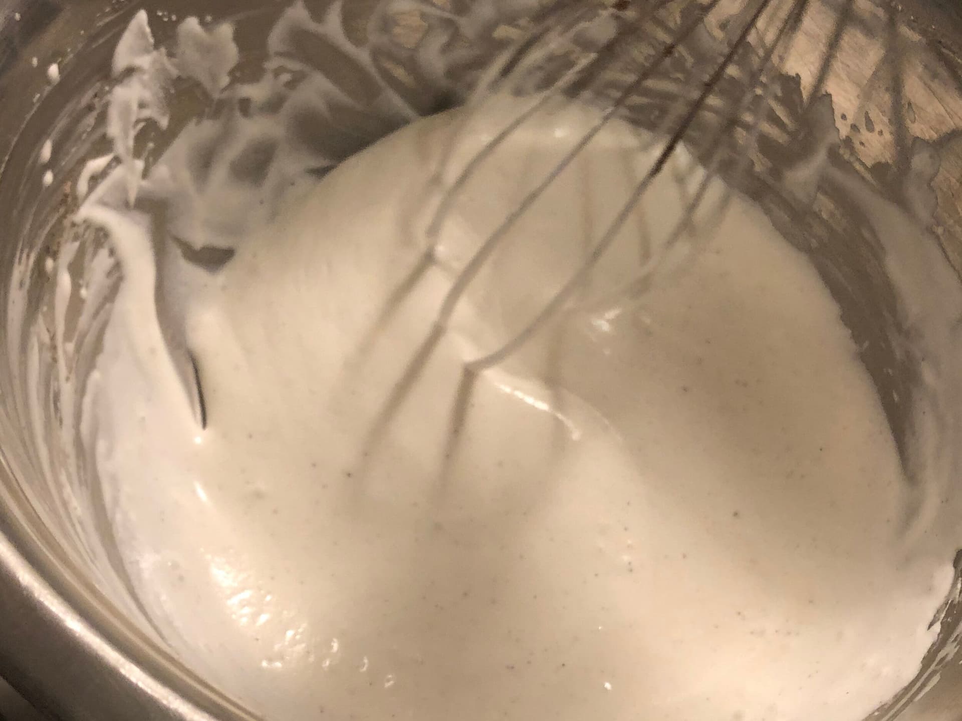 Soft peaks of whipped cream being whisked in a glass bowl with a wire whisk.
