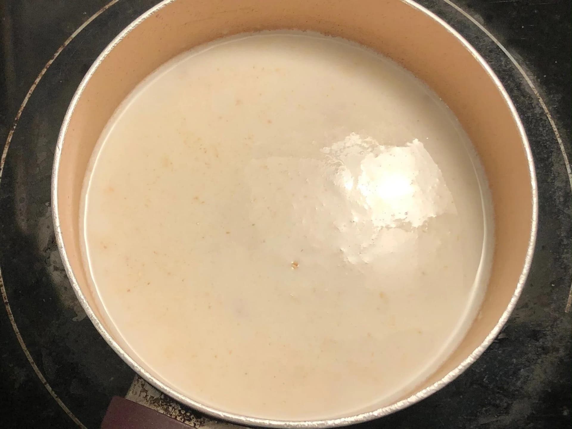Oats and milk simmering in a pot on the stove, showing a creamy beige mixture with visible specks.