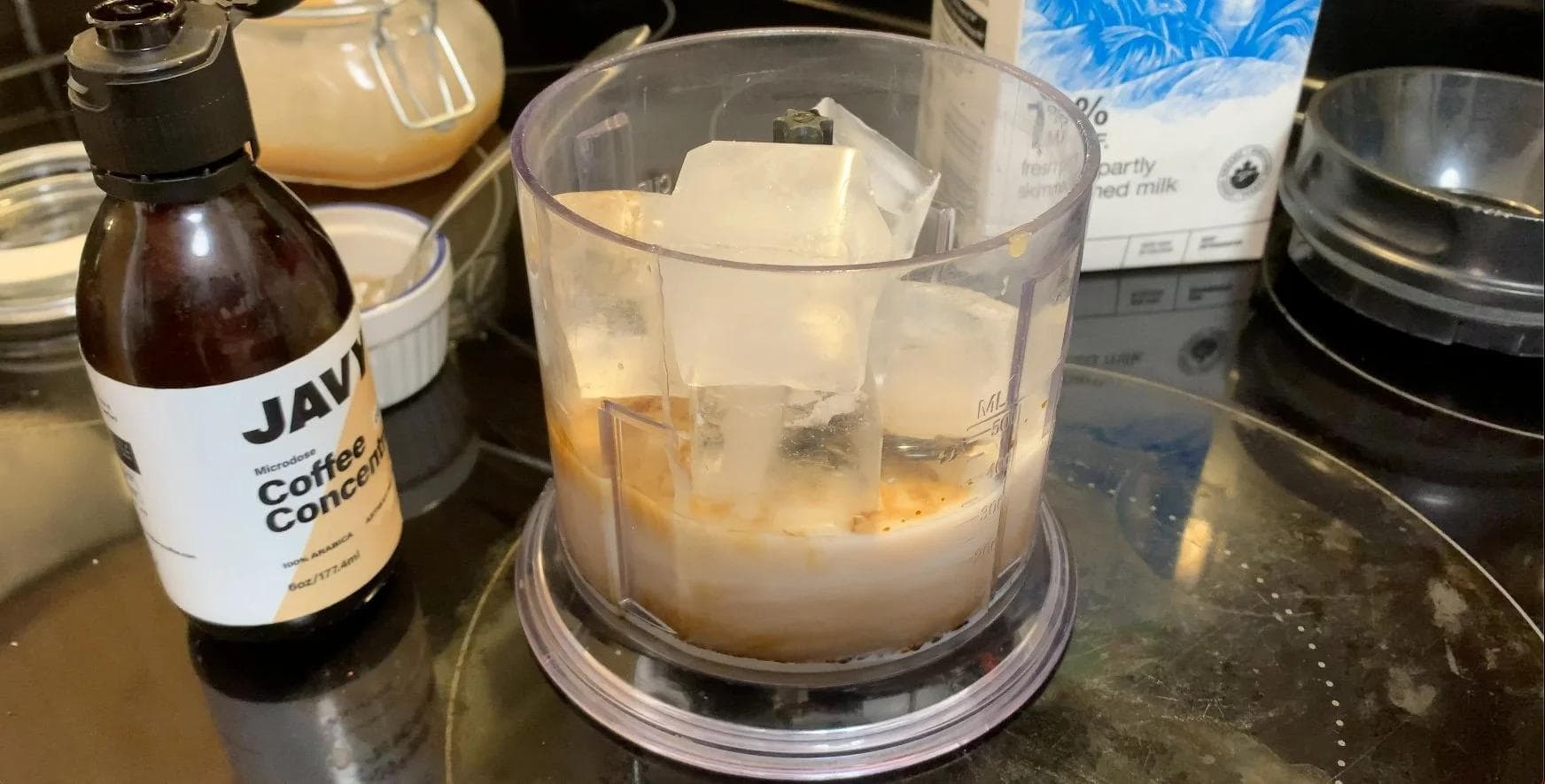 Blender filled with milk, ice, Javy coffee concentrate, vanilla syrup, and caramel sauce before blending for frappuccino.