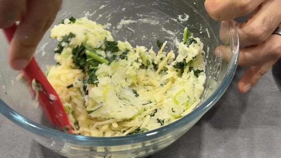 Mashed potatoes mixed with chopped green onions and chives in a glass bowl, ready to be seasoned.