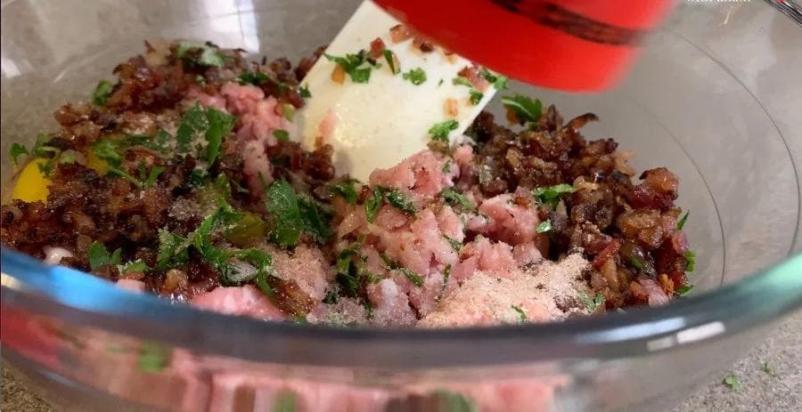 Raw pork and bacon sausage mixture in a glass bowl with fresh parsley and seasonings ready to cook.