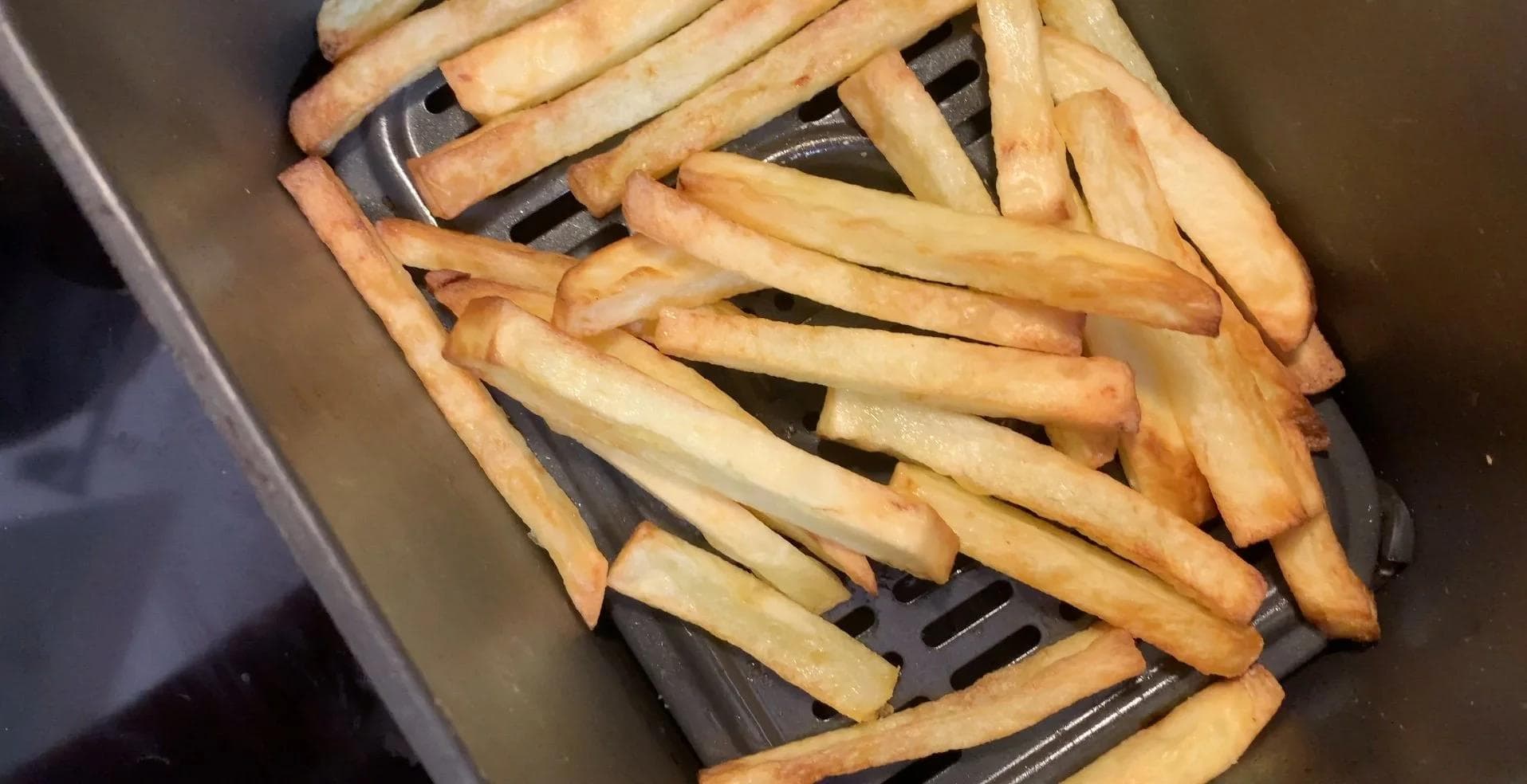 Golden crispy fries in an air fryer basket during cooking.