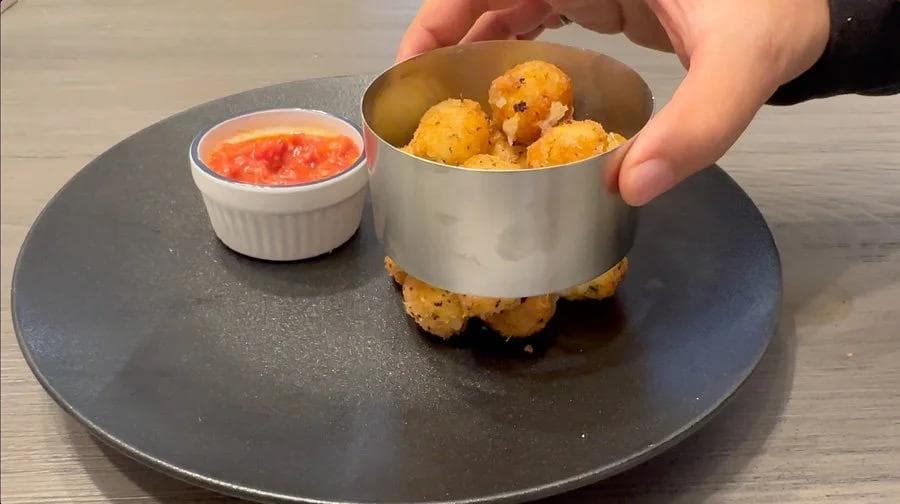 Fried mozzarella balls in a metal cup with marinara dipping sauce, served on a dark plate.