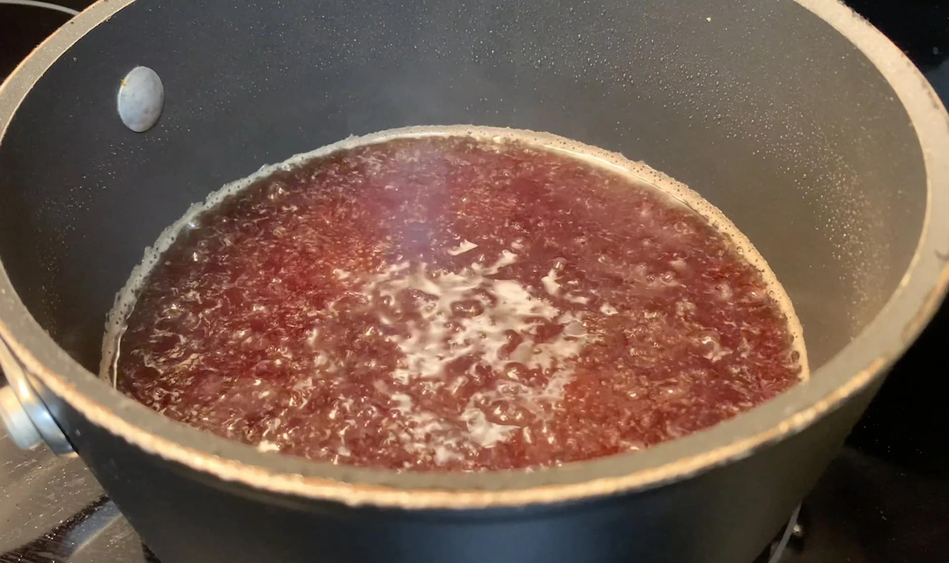 Pomegranate juice simmering gently in a dark sauce pan on the stovetop.