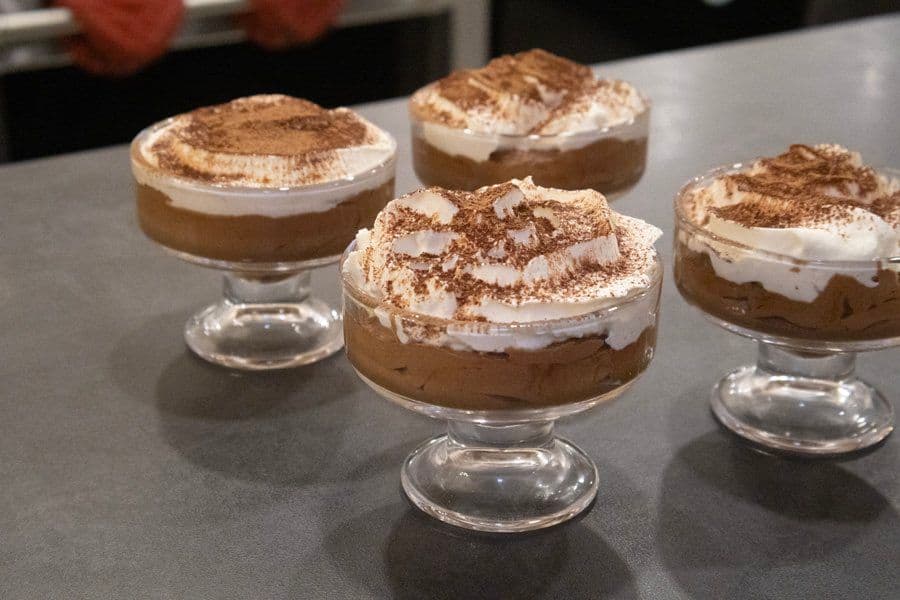 Five chocolate mousse desserts in glass cups topped with whipped cream and cocoa powder.