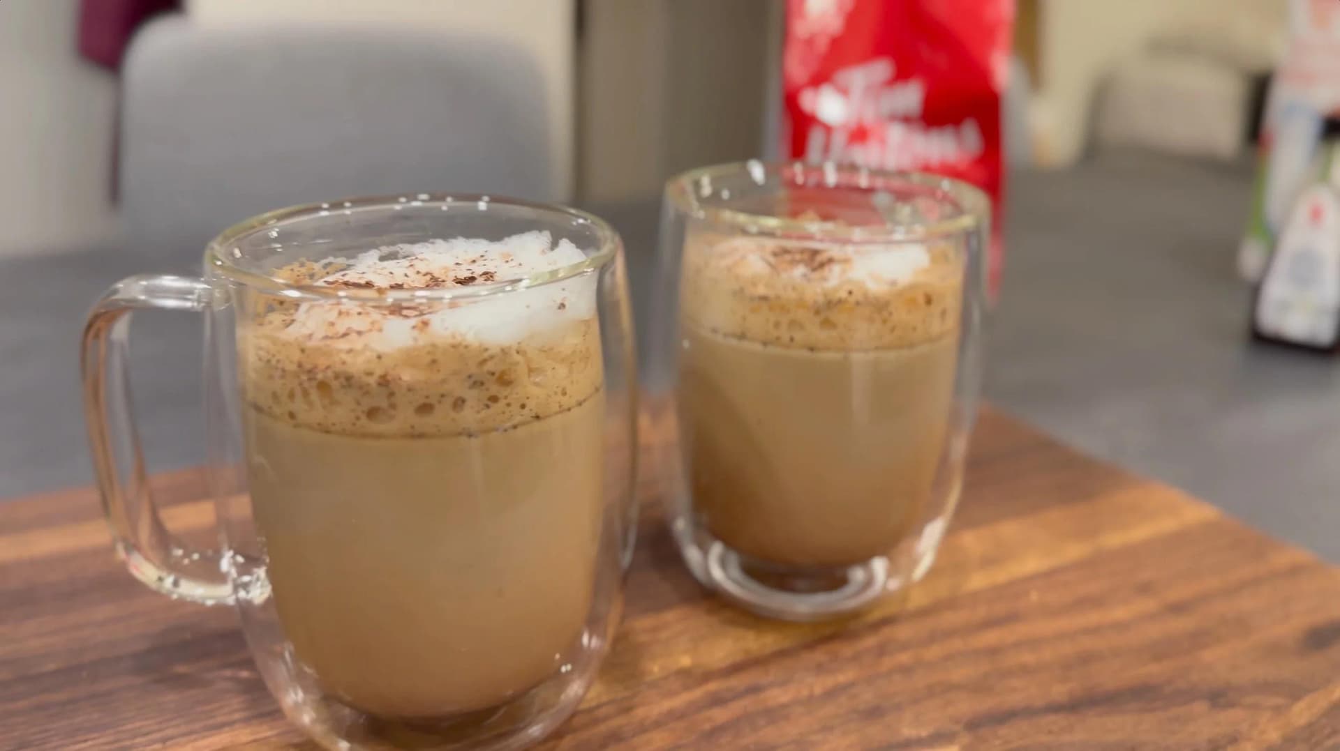 Two glass mugs of cocoa cappuccino with creamy tan liquid and cocoa powder sprinkled on top.