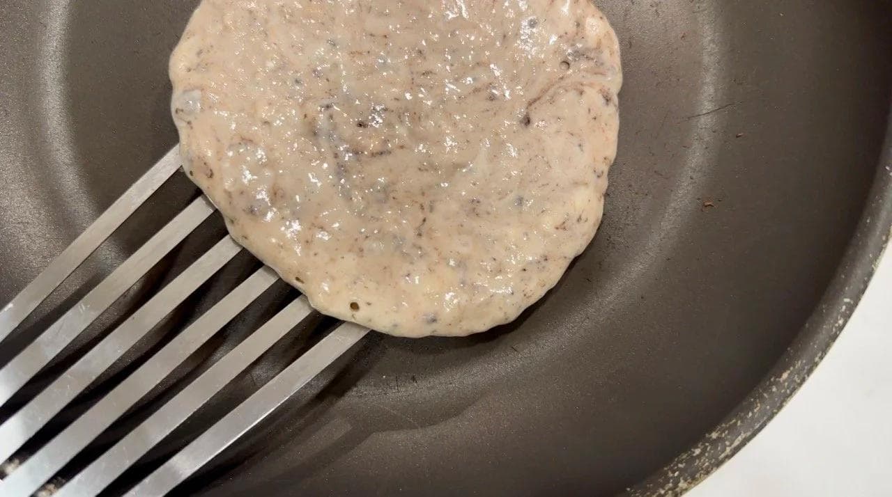 Gluten-free pancake batter cooking on a non-stick skillet with a spatula, showing bubbles forming on the surface.