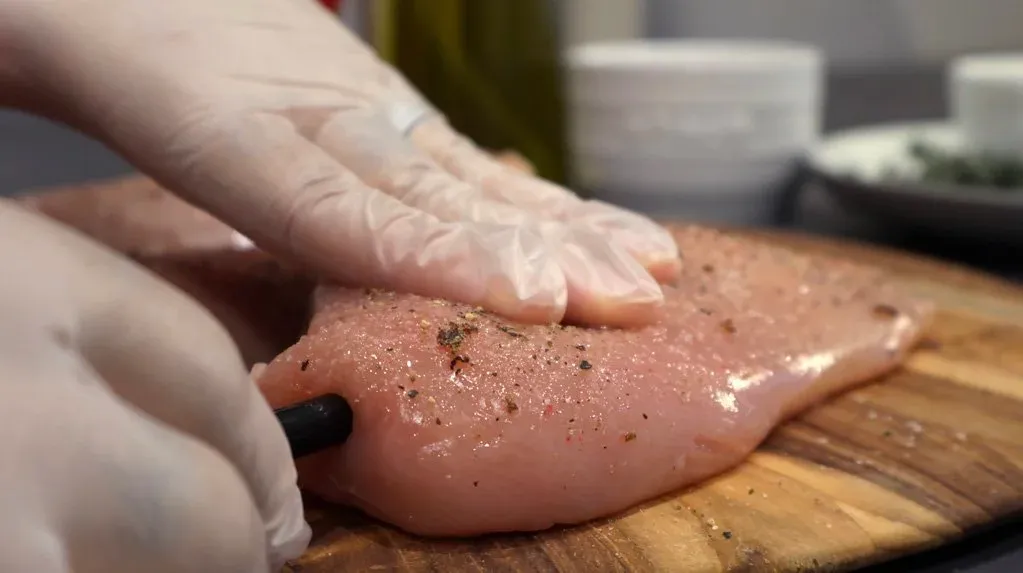 Seasoned chicken breast being patted dry with a paper towel on a wooden cutting board.