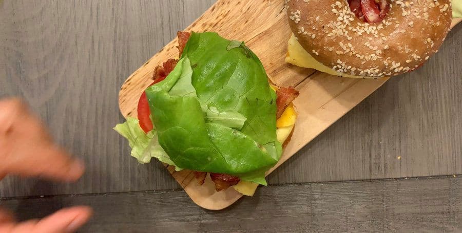 Assembled avocado BELT bagel sandwich with mashed avocado, fresh lettuce, egg, tomato, and bacon on a toasted seeded bagel.