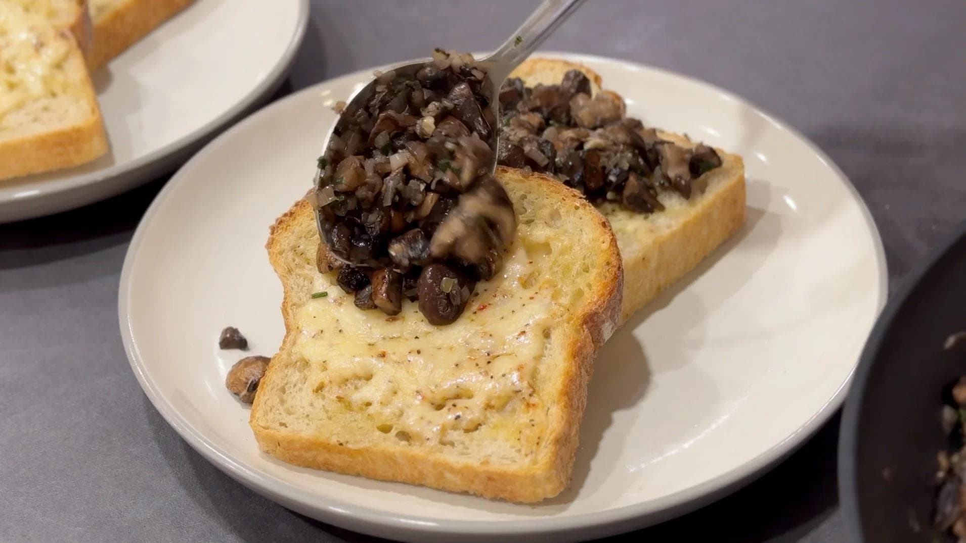 Sautéed mixed mushrooms served over toasted sourdough bread on a white plate, topped with cheese.