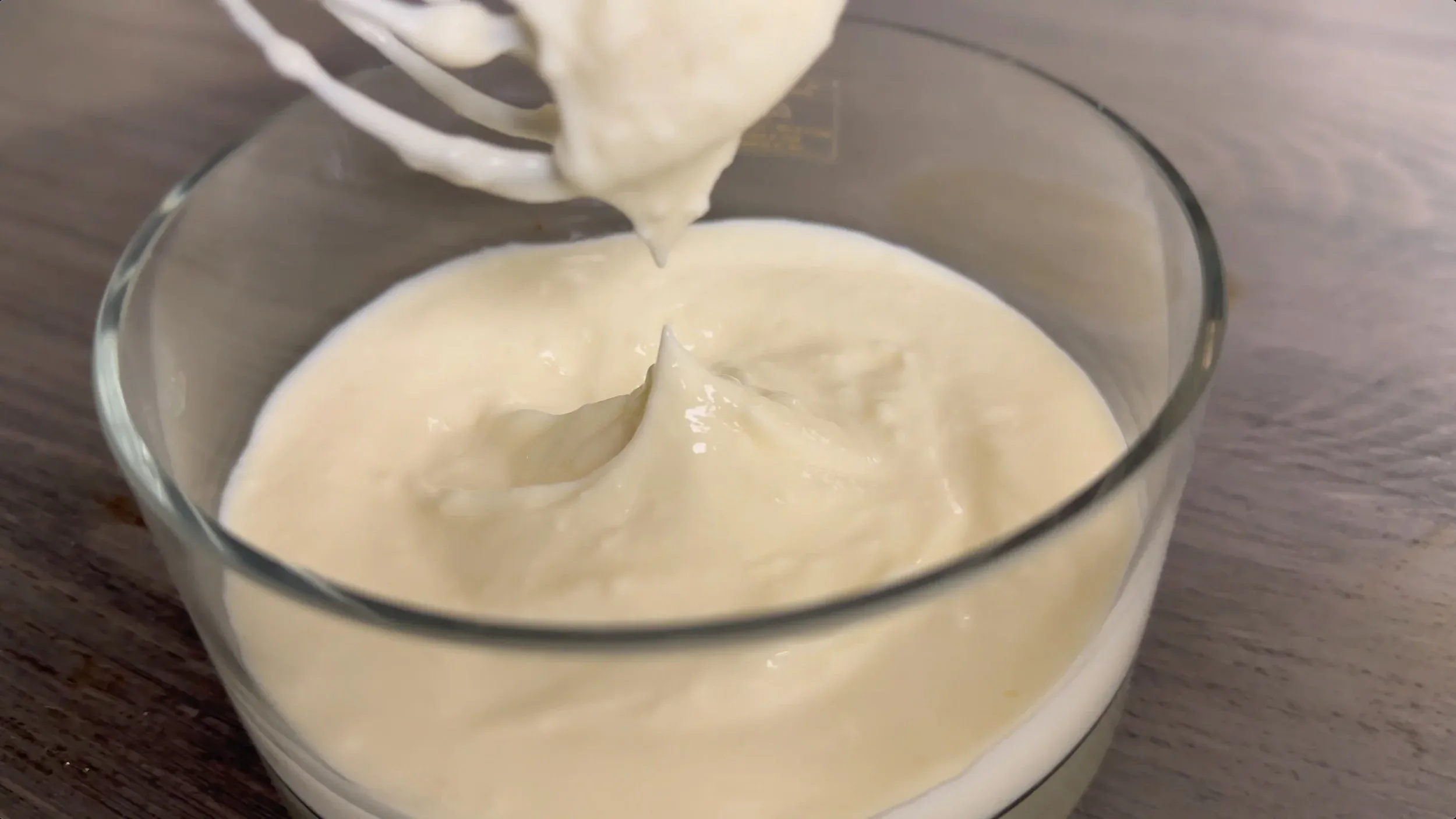 Cream cheese glaze being poured into a glass bowl, showing its smooth, thick consistency.