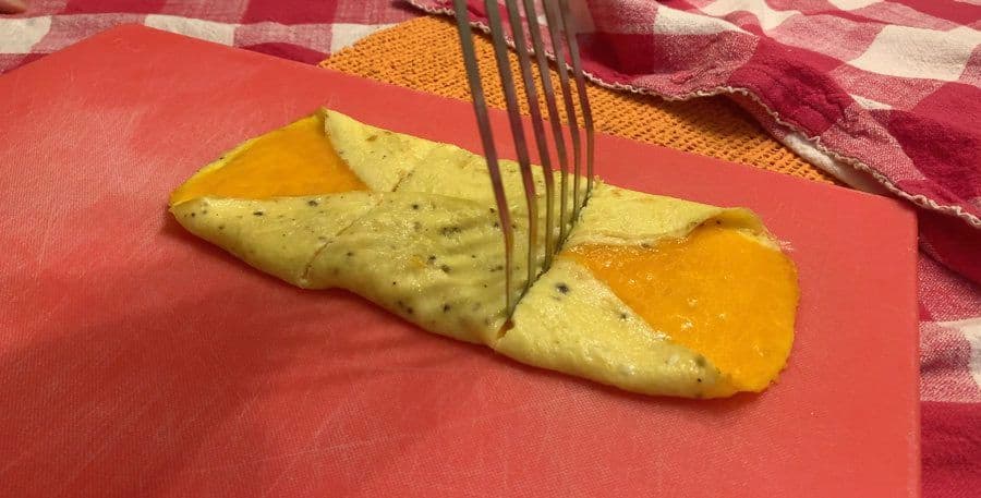 Folded omelette with melted cheese on a red plate, being cut with a fork.