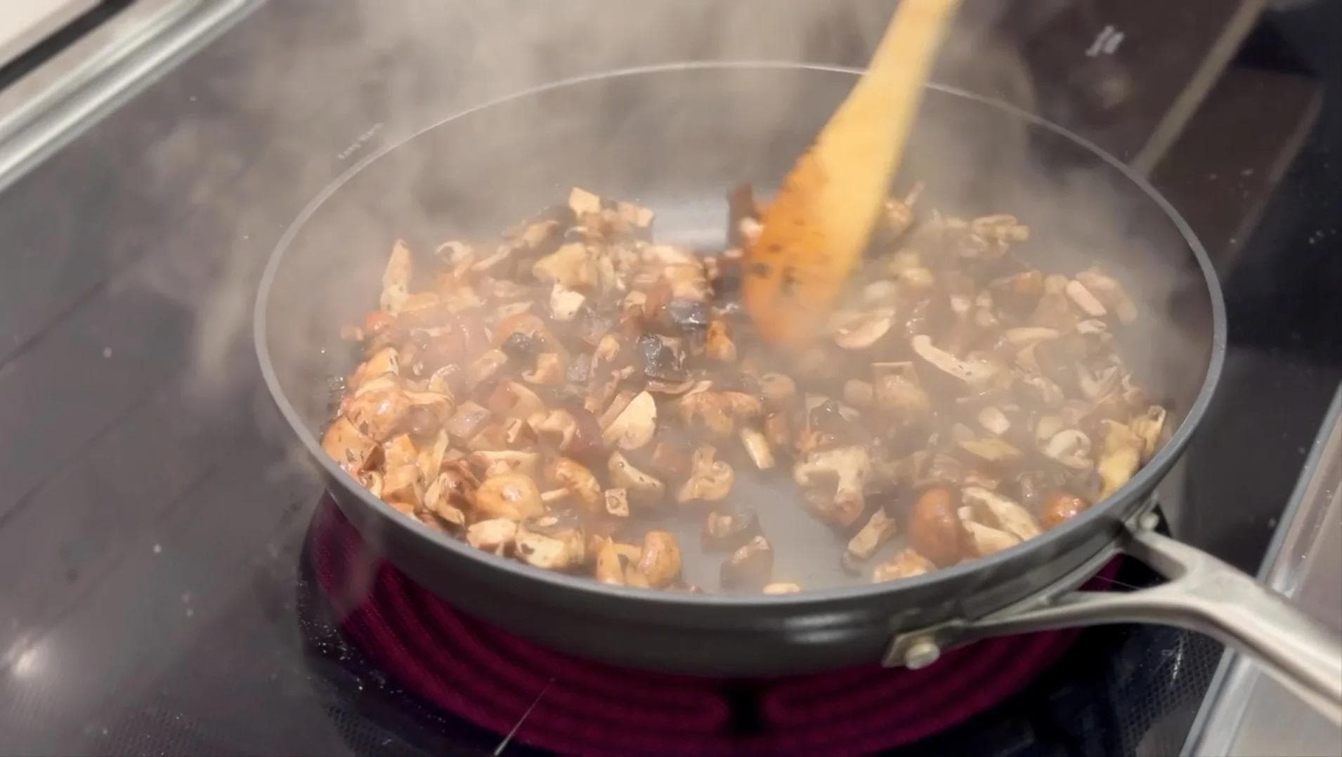 Diced mushrooms cooking in a pan with a wooden spoon, releasing moisture while steaming.