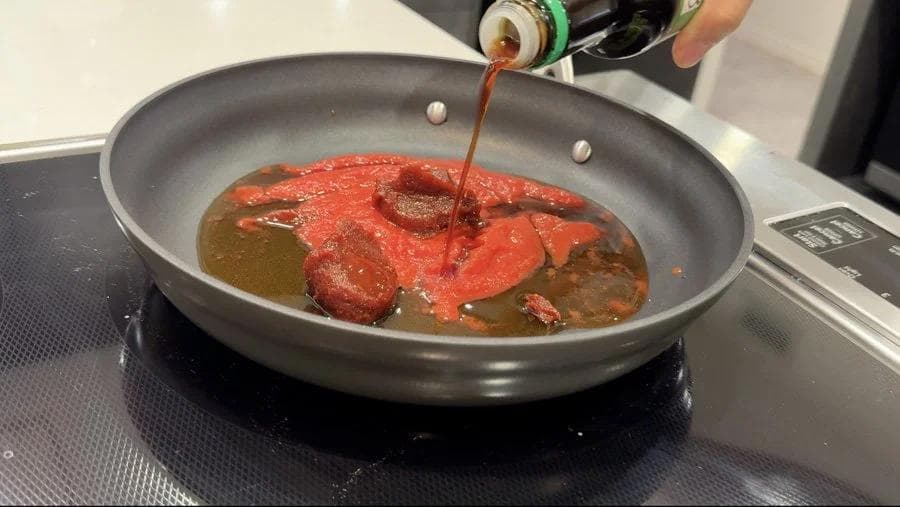 Korean sauce being poured into a pan with red tofu pieces and oil simmering on a stovetop.