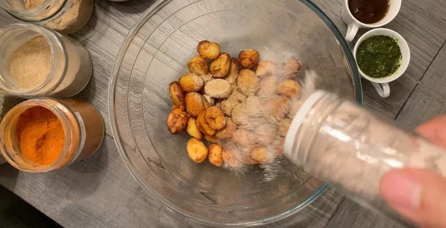 Crispy golden air-fried baby potatoes being tossed with dry spices in a glass bowl.
