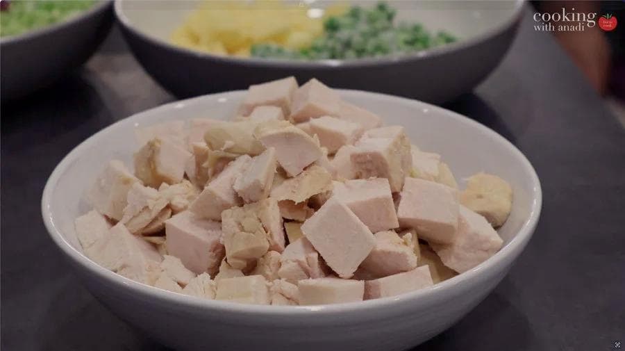 Diced chicken pieces in a white bowl, cut into small cubes for the pot pie filling.