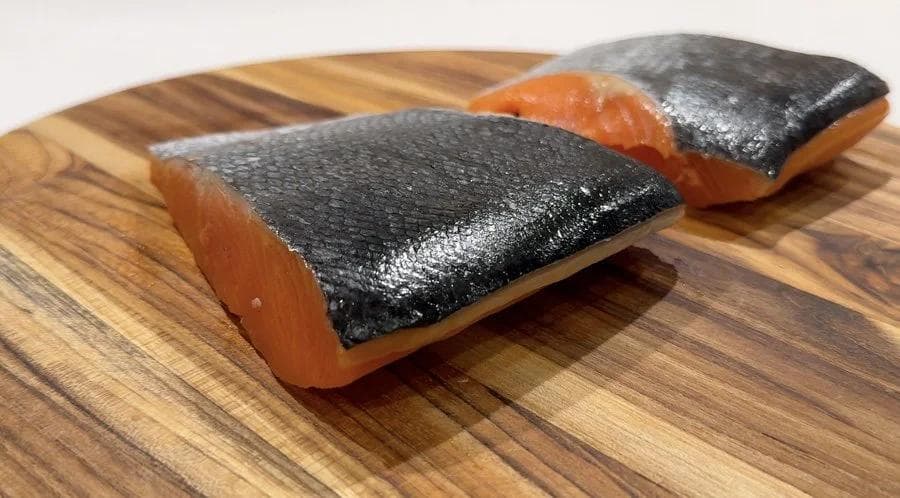 Two salmon fillets with skin on, placed skin-side up on a wooden cutting board.