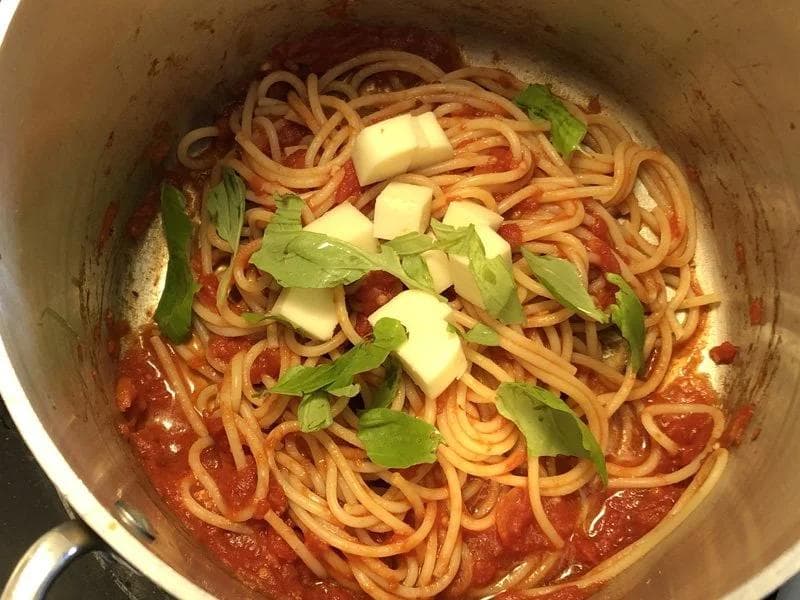 Spaghetti in tomato sauce topped with mozzarella cubes and fresh basil in a pot.