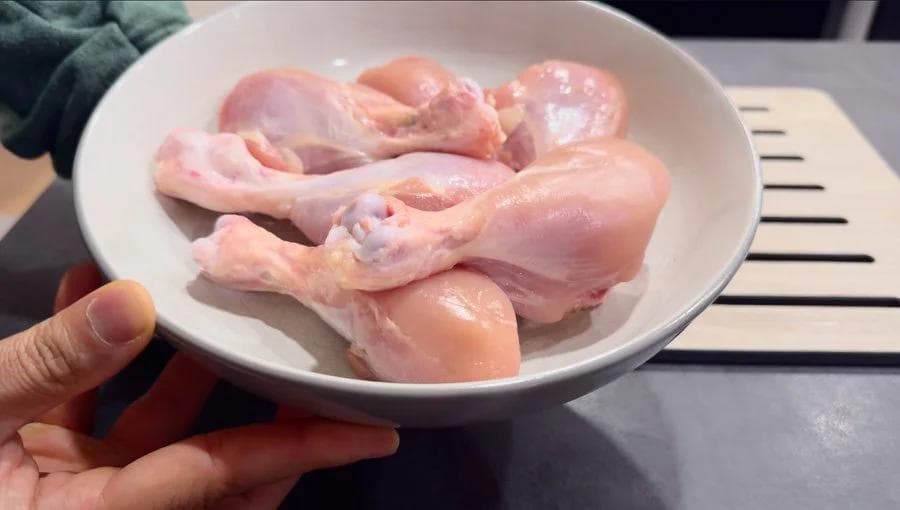 Raw chicken pieces with gashes in a white bowl ready for marinating with lemon juice and spices.