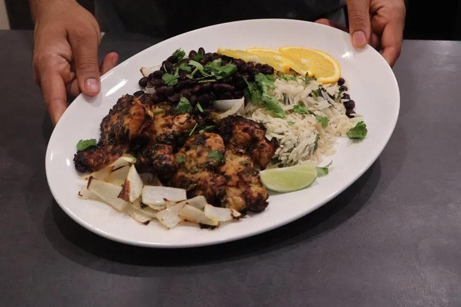 Cuban mojo chicken plated with black bean salad, white rice, plantain chips, and lime wedge garnish.