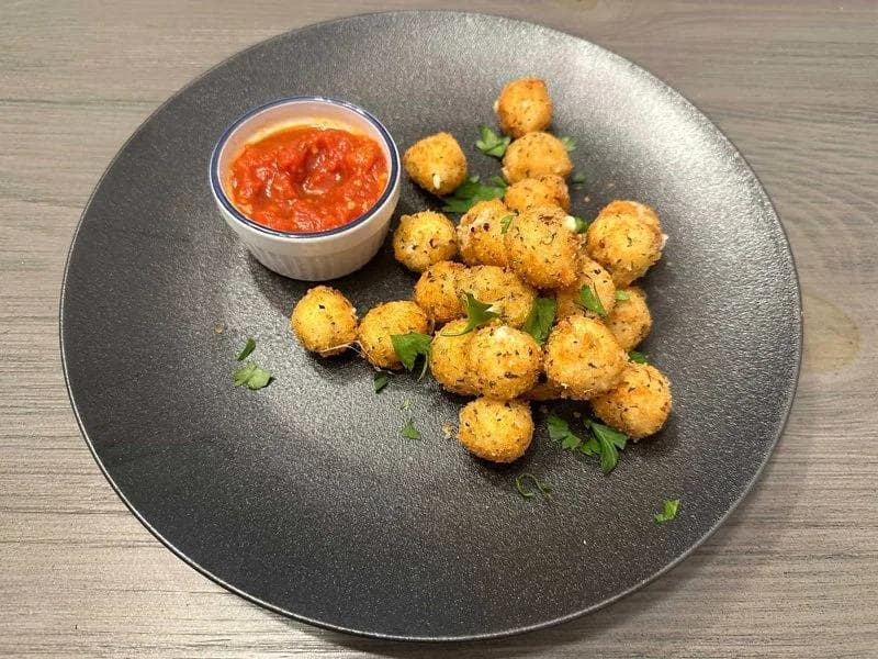 Crispy fried mozzarella balls on a dark plate with red dipping sauce and fresh parsley garnish.